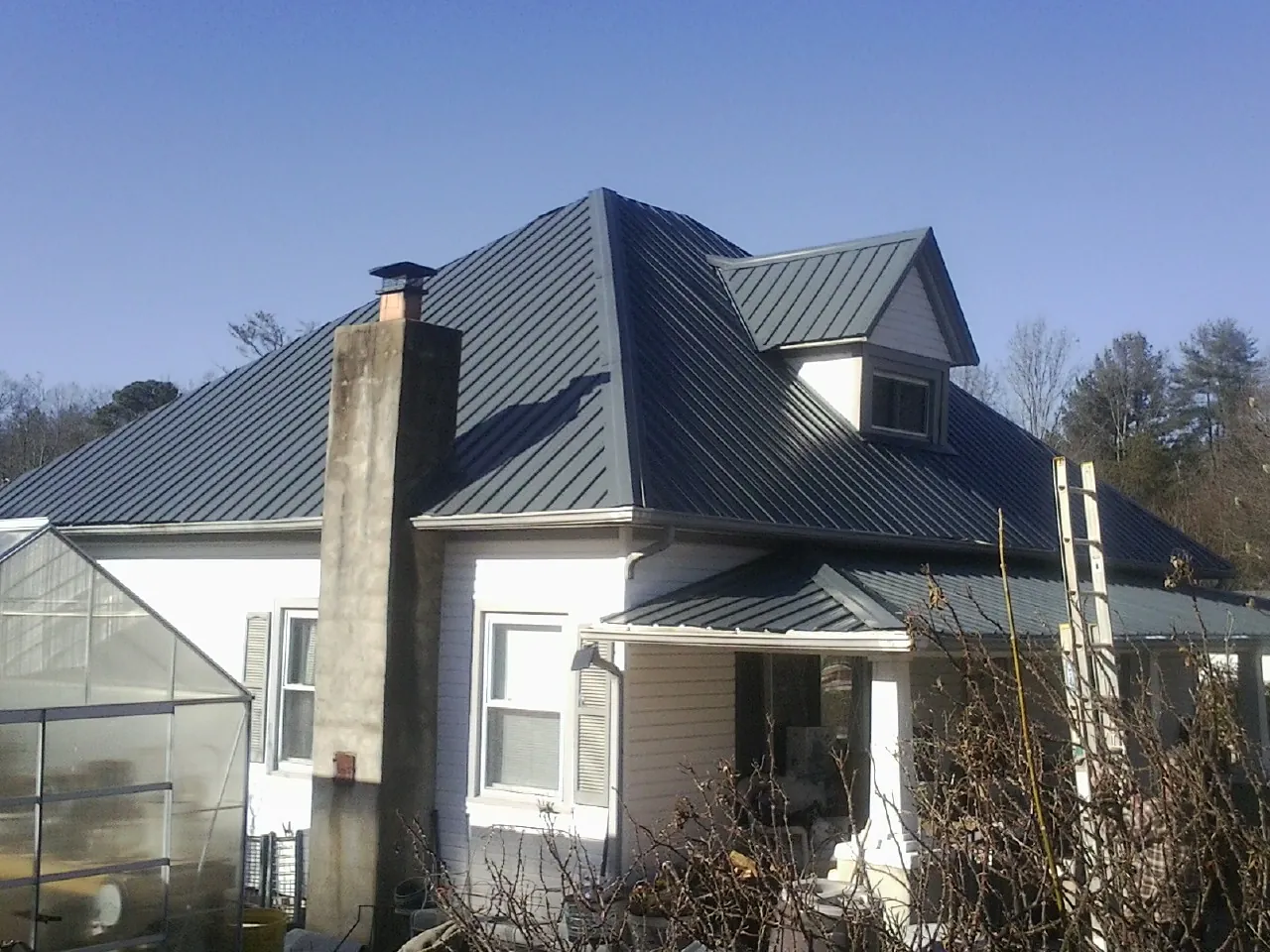 Dark blue standing seam metal roof on a white farmhouse with dormer — Slate & Tile Roof Repair by Roofing Brothers in New Richland