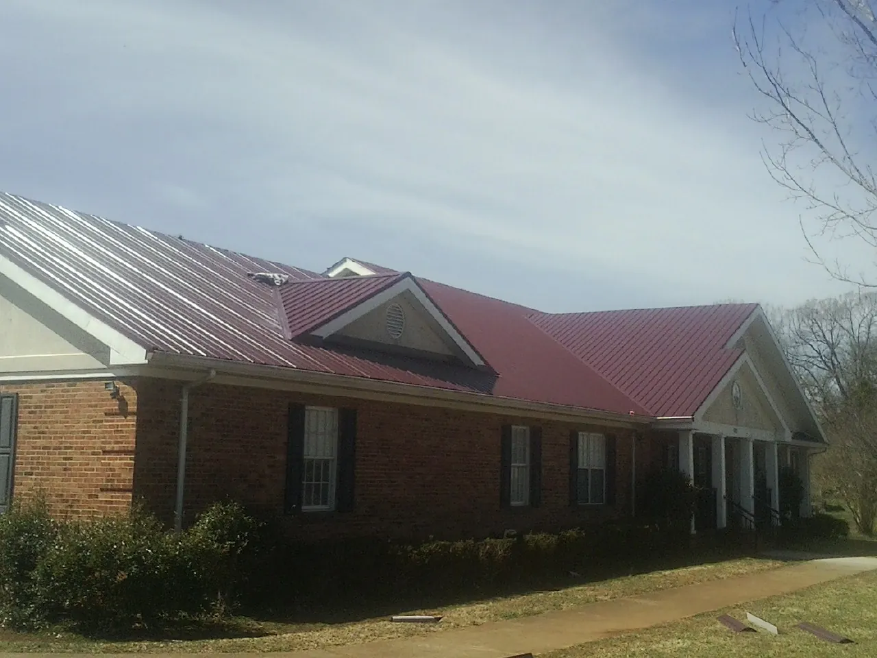 Red metal roof with gabled entries on a long brick building, from a Hail Damage Roof Repair job in New Richland