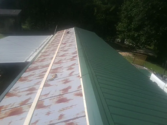 Old rusted panels beside newly installed green metal roofing — Wind Damage Roof Repair by Roofing Brothers in New Richland
