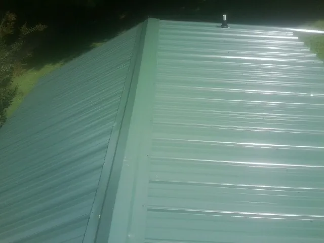 New green metal panels meeting at the ridge of a roof — Flat Roof Repair work by our crew in New Richland