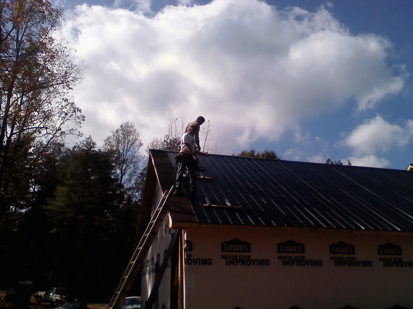 Roofer fastening dark metal panels high against a cloudy sky, from a Roof Inspection job in New Richland