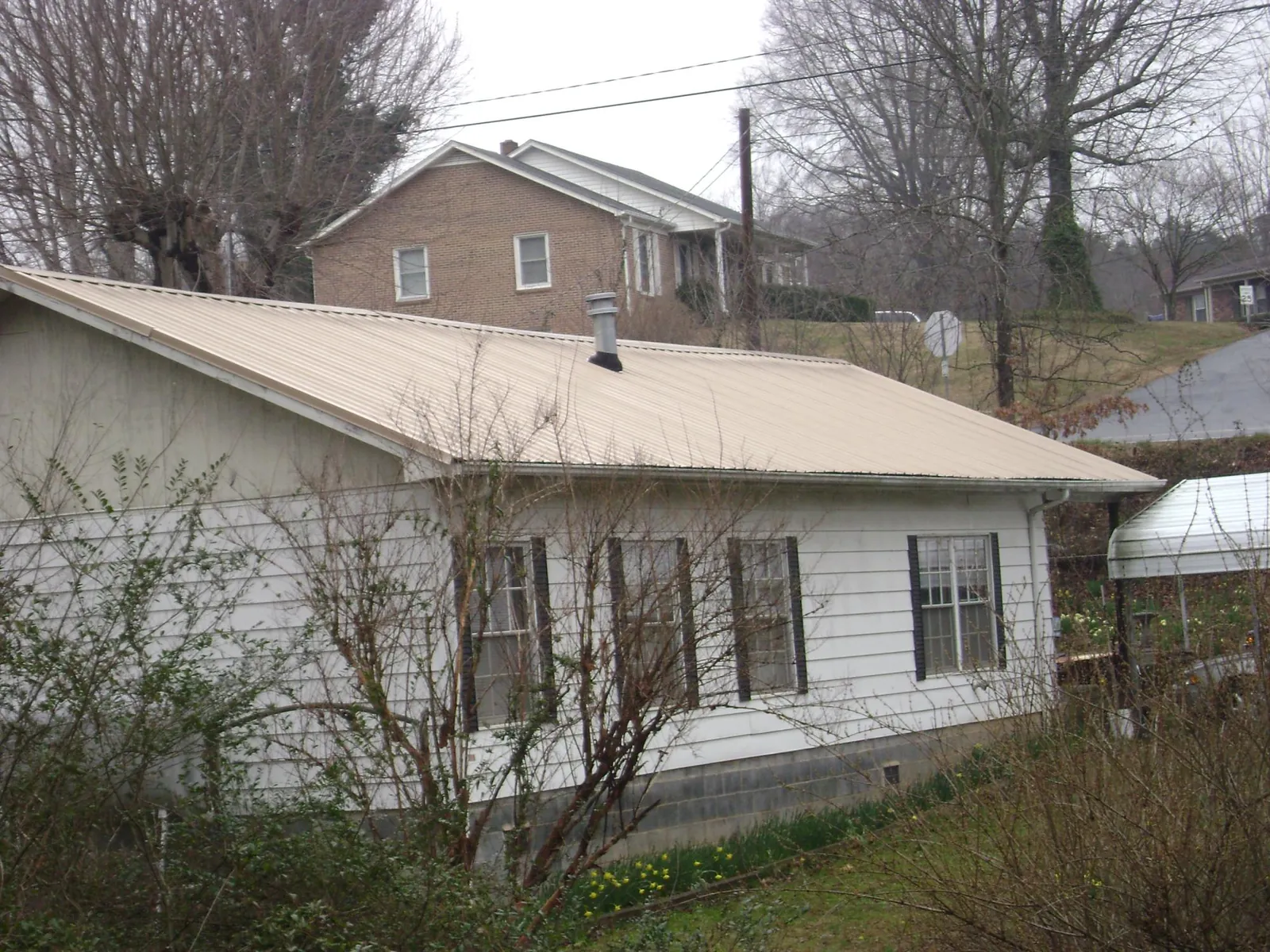 Tan metal roof on a white sided house set into a hillside — Commercial Roofing by Roofing Brothers in New Richland